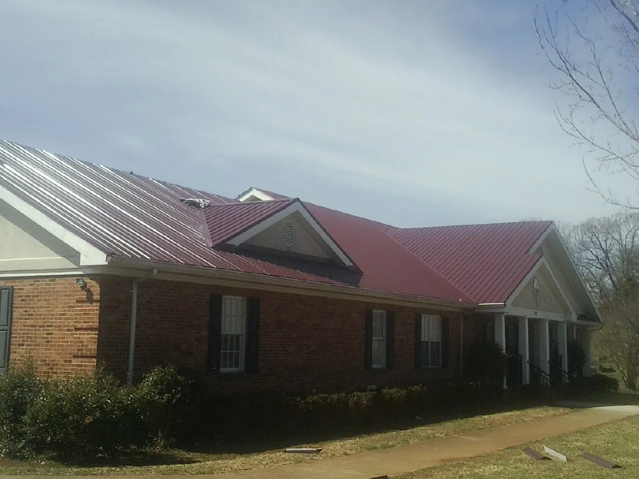 Red metal roof with gabled entries on a long brick building, from a Hail Damage Roof Repair job in Hawk Point