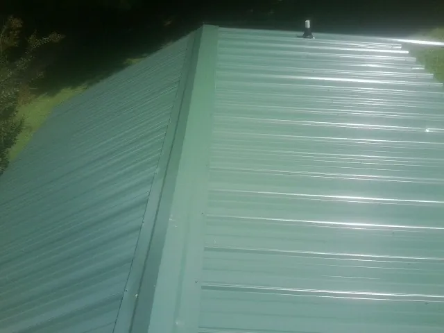 New green metal panels meeting at the ridge of a roof — Flat Roof Repair work by our crew in Hawk Point