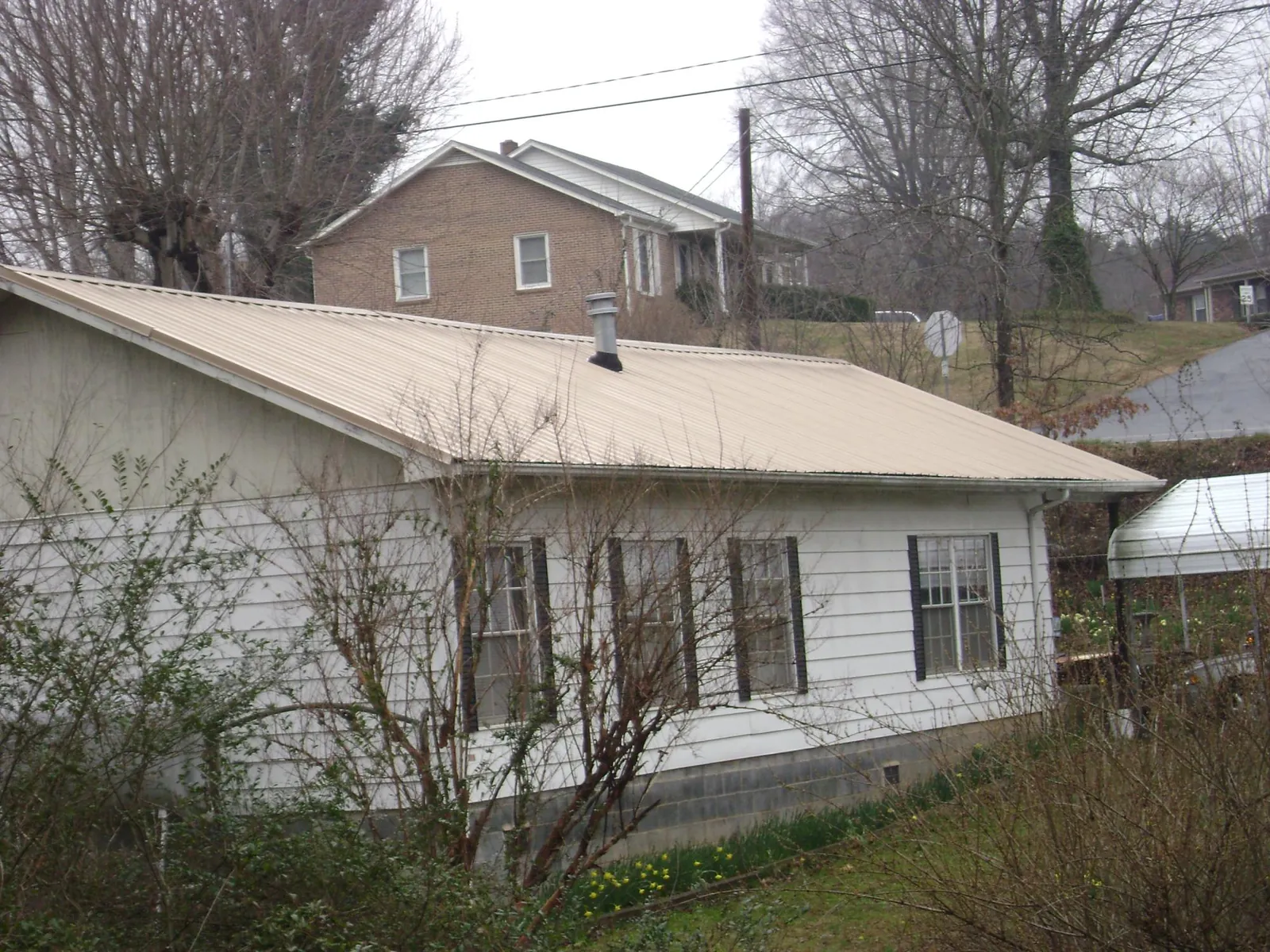 Tan metal roof on a white sided house set into a hillside — Commercial Roofing by Roofing Brothers in Hawk Point